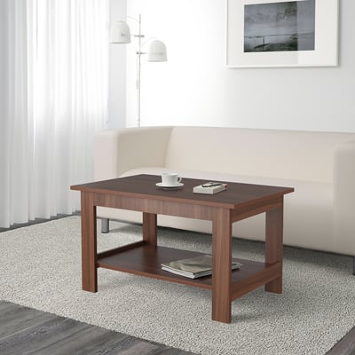 Wooden coffee table with two shelves. Top shelf holds a cup and remote. Bottom shelf holds magazines.
