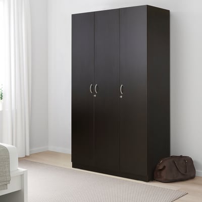 Black NODELAND wardrobe, tall & sleek, beside white bed, with brown bag.