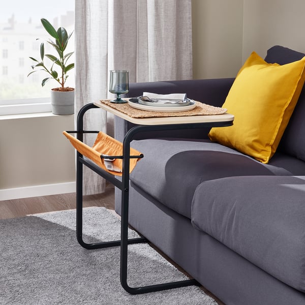 Black metal side table with wooden top and yellow pillow on sofa by window.