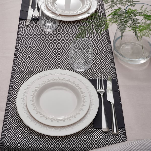 Two dinner settings with stacked white plates, silverware, and clear glasses on a patterned runner.