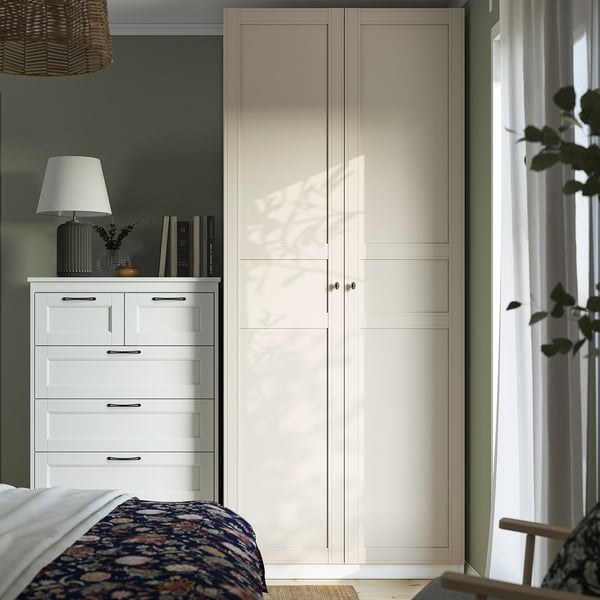 Modern bedroom with white PAX wardrobe, tall and narrow; next to a dresser, partially covering curtains; blue patterned bedding.