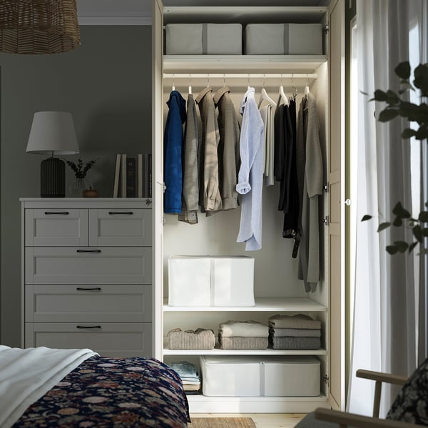 A modern bedroom with an open wardrobe showcasing clothes, storage boxes, and interior lighting.