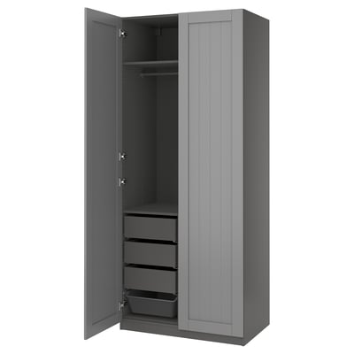 A grey PAX wardrobe with open doors revealing shelves and drawers. The modern design includes adjustable feet and soft-closing hinges.