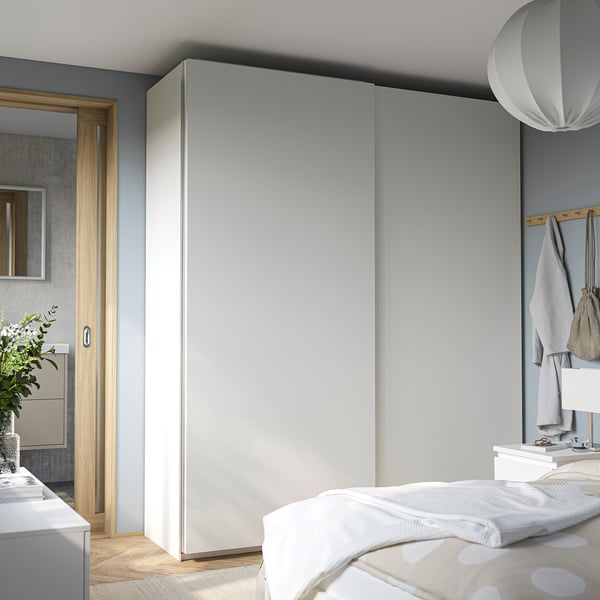 Bedroom with large grey PAX wardrobe, sliding doors, white bed, and mirror. Minimalist design, light wood floors.