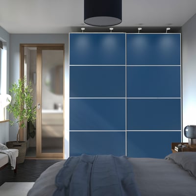 Modern bedroom with large blue PAX wardrobe, grey bed, and plant near entrance.