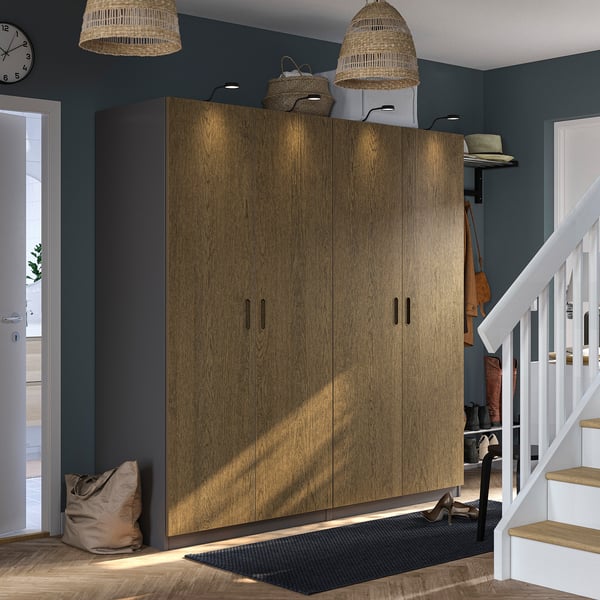 Large wooden PAX wardrobe, tall and wide, fits entry with stairs. Dark floor, bright walls, wicker lamps overhead.