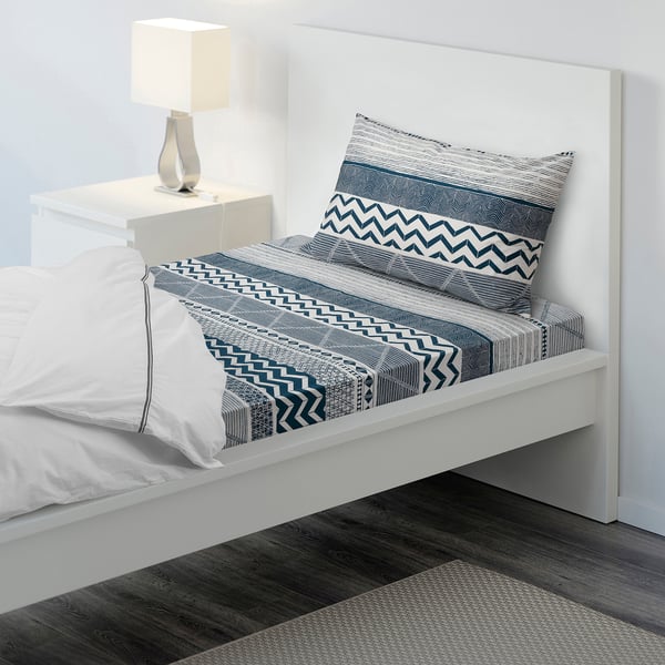 Bed with white & blue patterned sheet, single pillow, bedside lamp, modern design, fits neatly by wall.