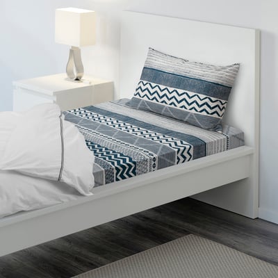 Bed with white & blue patterned sheet, single pillow, bedside lamp, modern design, fits neatly by wall.