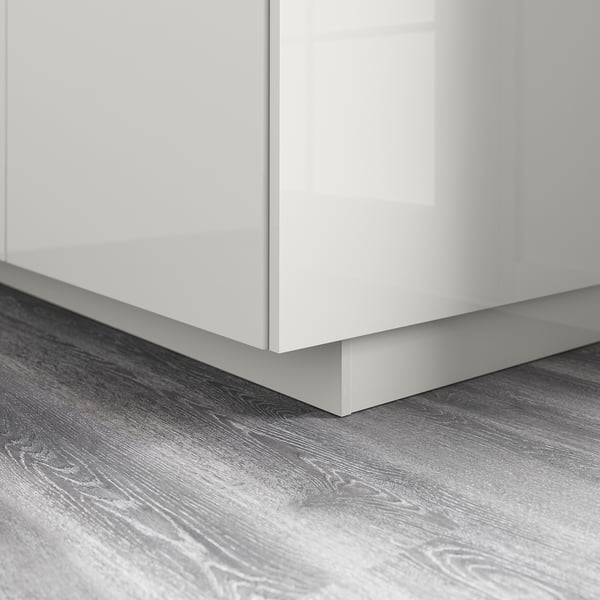 A glossy white cabinet base with grey wooden flooring. The cabinets sleek design repels moisture and dirt, ensuring a clean and modern look.