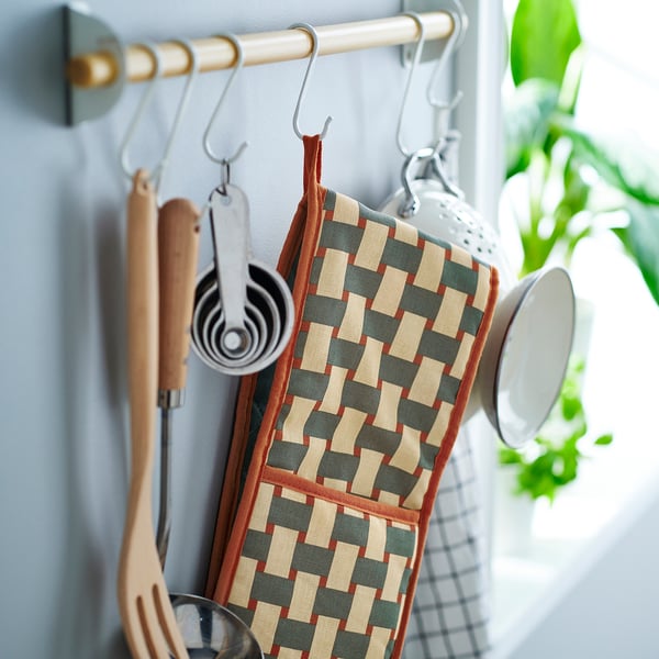 Kitchen scene: colourful oven mitt hangs with utensils on a wall rack.