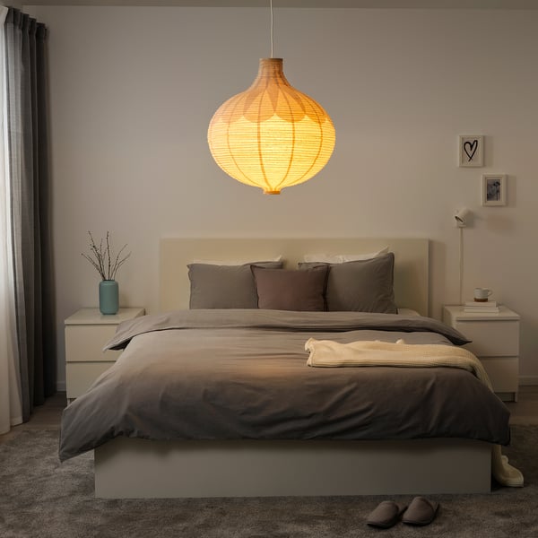 Bedroom with large hanging light. Bed has grey bedding, nightstands with items, curtains on side.