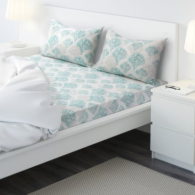 White & teal cotton bedding set, standard size, leaf pattern, dark wood floor, rug, bedside table.