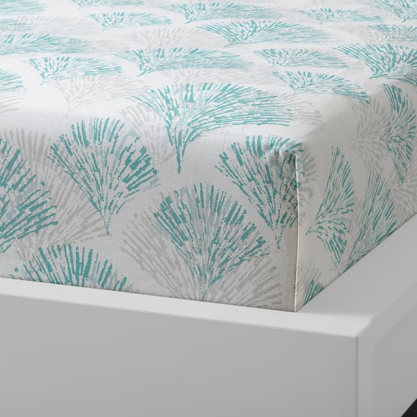 A bed sheet with a green, leafy pattern on a white background, made of 100% cotton, displayed on a white bed.