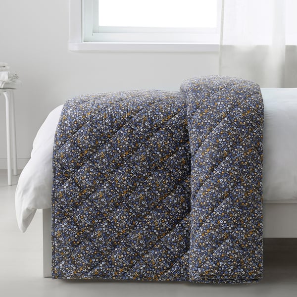 A dark blue comforter with tiny flowers is draped over a bed, providing soft, cosy warmth. The floral pattern creates a romantic atmosphere.