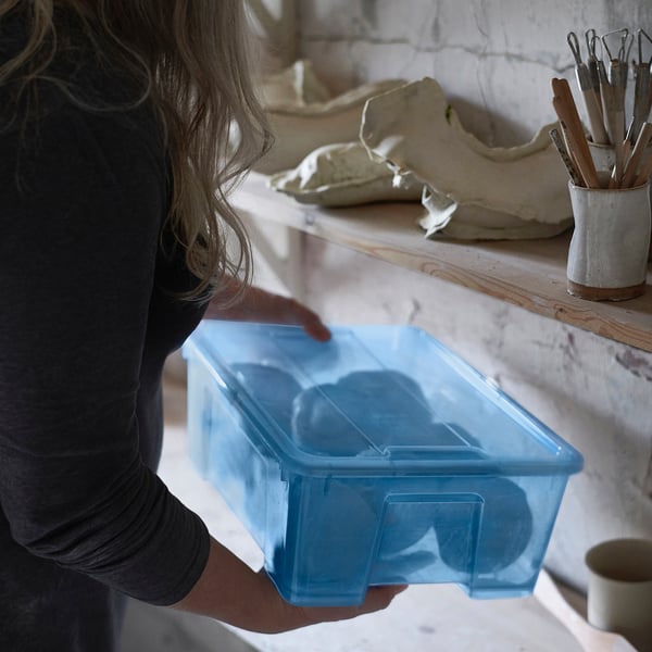 A person holding a blue, medium-sized SAMLA box near art supplies.