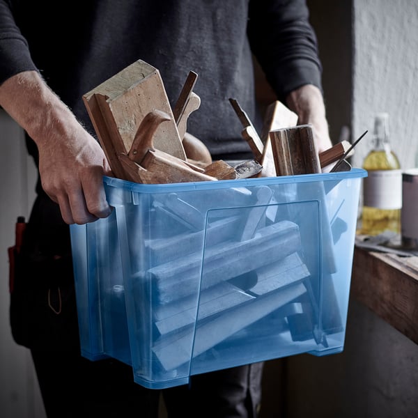 Person carrying a blue storage box filled with various wooden tools and pieces. Transparent sides for easy visibility.