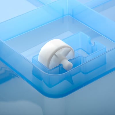 A clear, blue plastic storage box with wheels holding a white, spherical object.