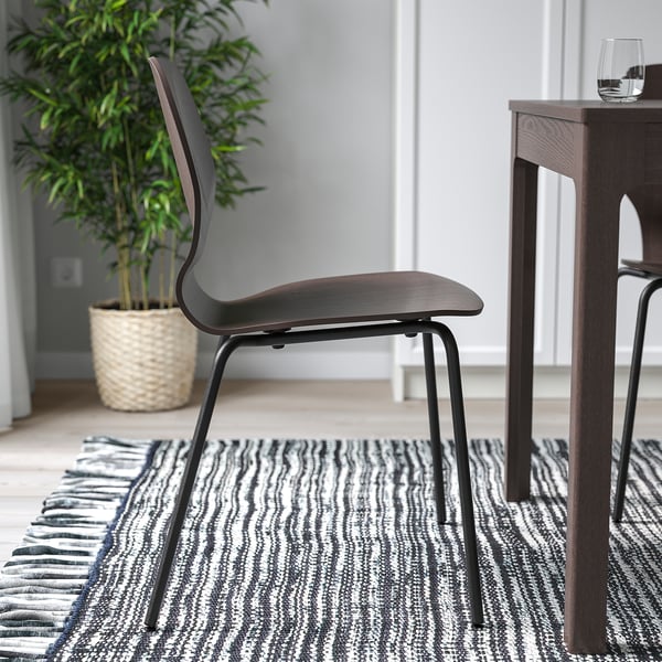 Dark wooden chair with metal legs on a striped rug near a table with a glass of water and a potted plant.