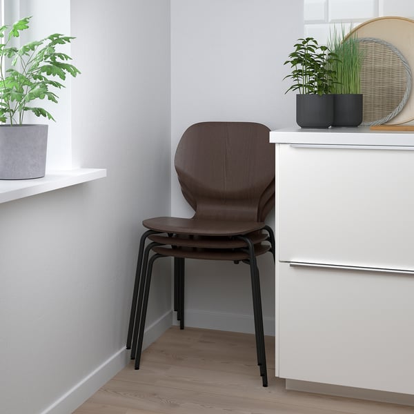 Stackable wooden chair with black metal legs, positioned under a shelf with potted plants.