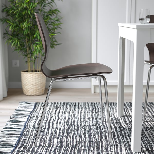 A modern chair with a curved seat and metallic legs sits on a striped rug, beside a white bar table with a wine glass.