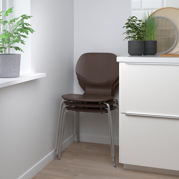Wooden chair with chrome legs under white cabinet, lumbar support, minimalist setting with plants.