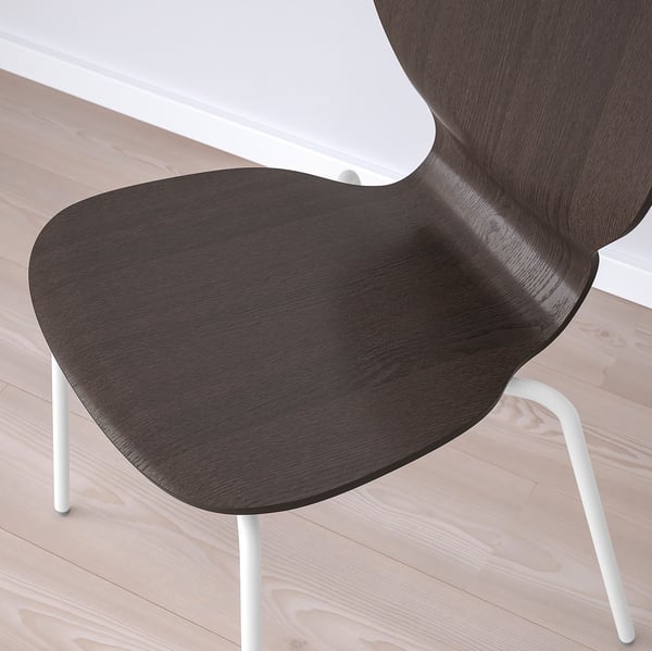 Dark wooden chair with sleek, curved design on light wooden floor. Comfortable seat and stylish white legs.
