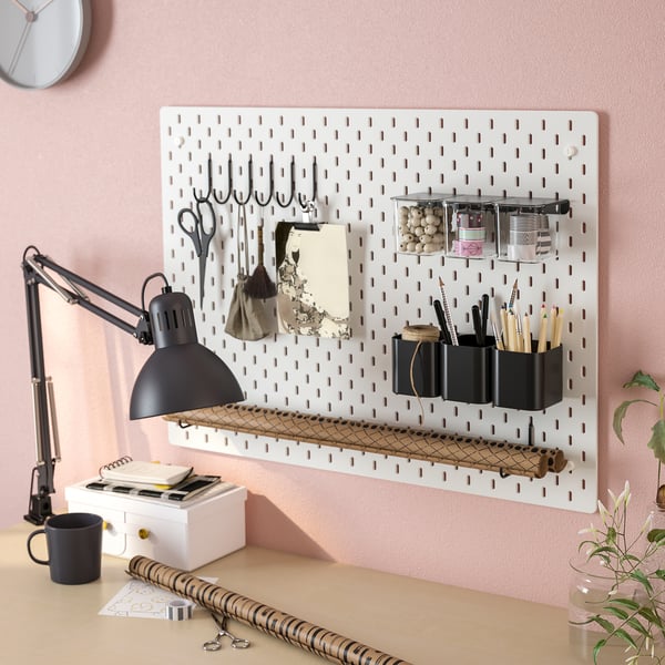 White pegboard with hooks, containers, scissors, lamp, and desk items organised on a pink wall.
