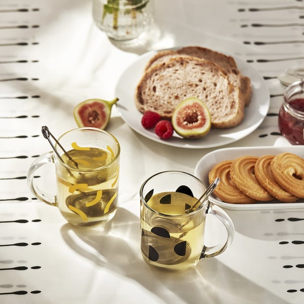 Glasses with lemon zest & handles on patterned tablecloth near food.