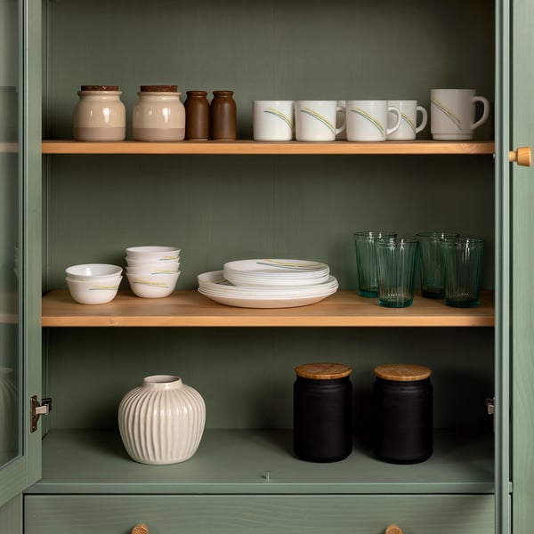 Green cabinet with wooden shelves holding white mugs, bowls, plates, and jars, organised neatly for space efficiency.