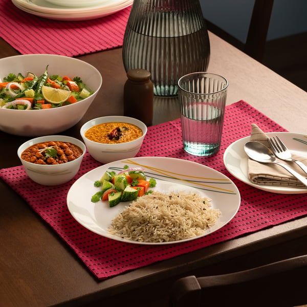 Table set with SKRÄNTÄRNA dinnerware: plates with rice and veggies, bowls with curry and salad, glass with water.