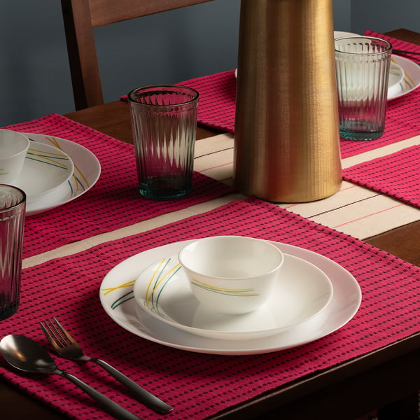 SKRÄNTÄRNA, clear rippled glasses next to colourful plates on a red placemat, perfect for elegant meals.