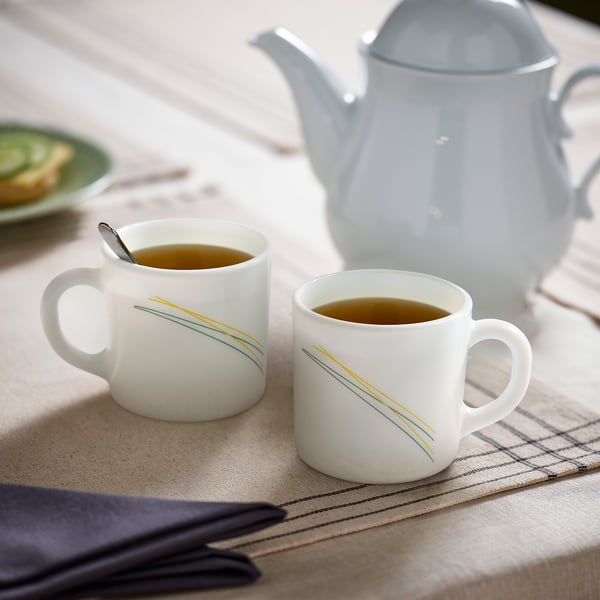 Two SKRÄNTÄRNA mugs with gold stripes by grey kettle; tea setting.