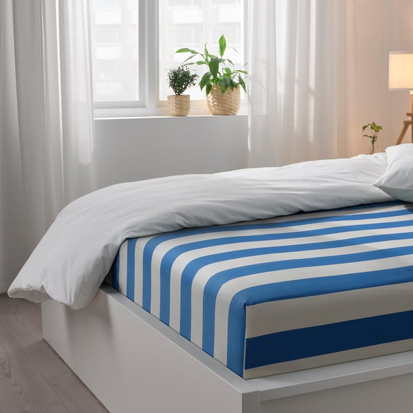 Bedroom with blue and white striped bedsheet, white pillows, and plants on window sill.