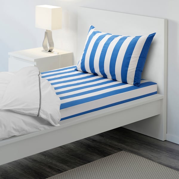 Blue and white striped bedding on a made bed, with a pillow, bedside table, and rug.
