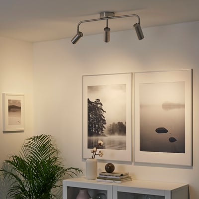 Modern room with ceiling lights, art prints, sideboard, and plant.