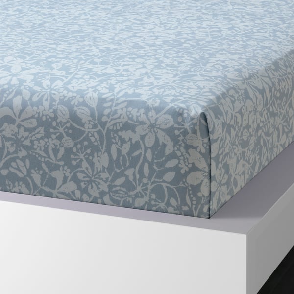 A neatly made bed with a floral-patterned sheet set in blue. The sheet is folded at the corner, showing its crisp, sateen weave.