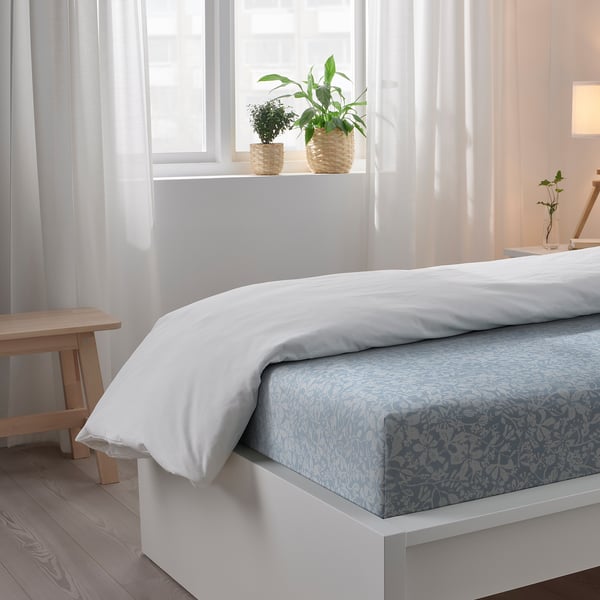 Bedroom with large window, white bedding with blue floral print, plants on windowsill.