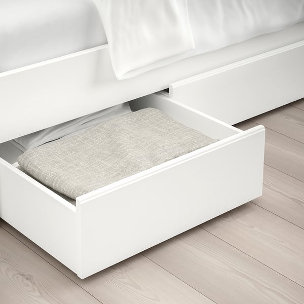 White bed frame with open drawer underneath showing folded grey blanket on wooden floor.