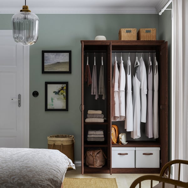 Bedroom with open wardrobe showing clothes, folded sweaters, handbags, and storage baskets; includes mirror door.