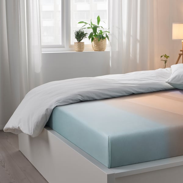 Bedroom with white curtains, window sill holding two potted plants, bed with blue and white bedding.