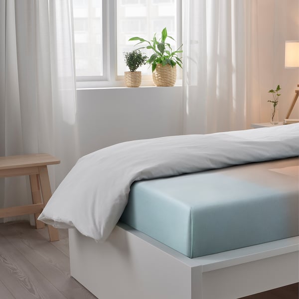 Bedroom with white bed sheets and light blue flat sheet, two plants on windowsill.
