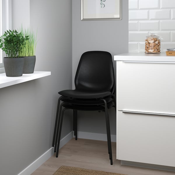 Black stackable STENSELE chair near white cabinets with potted plants.