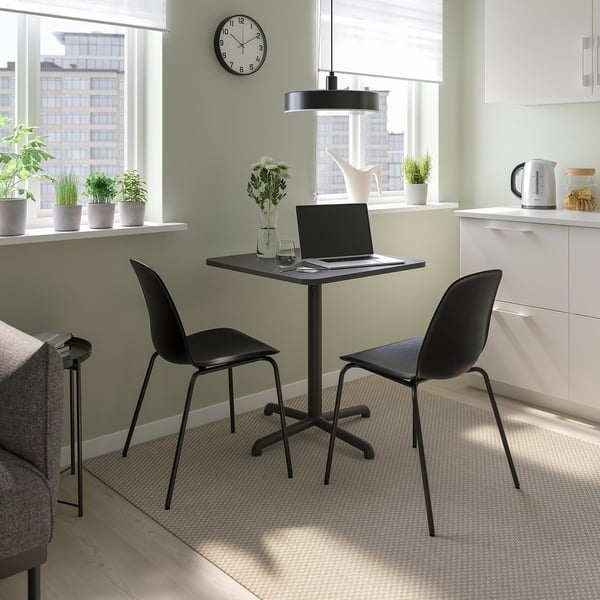 Small home office with STENSELE black table & chairs, laptop, plants, white wall, large window, kitchenette.