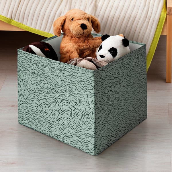 A fabric toy box with a green dot pattern holds stuffed animals under a bed.