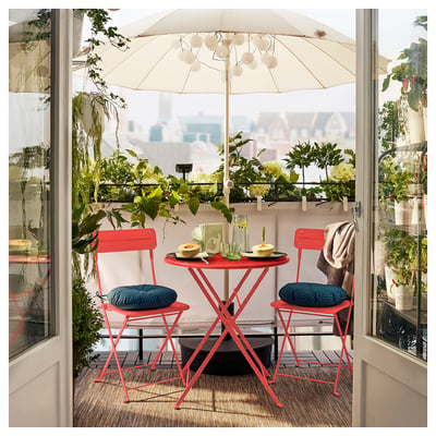 Bright red SUNDSÖ table & chairs set, folded for storage, perfect for small balconies with potted plants & city view.