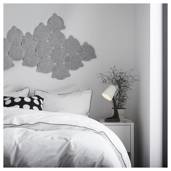 Modern bedroom with white bedding, black lamp, decorative wall art, and plant.