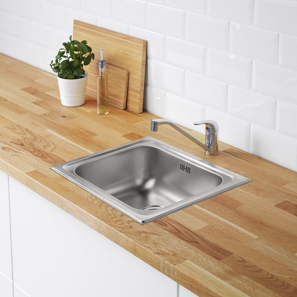 Modern kitchen with shallow stainless sink, slim tap. Small potted plant and oil bottle nearby.