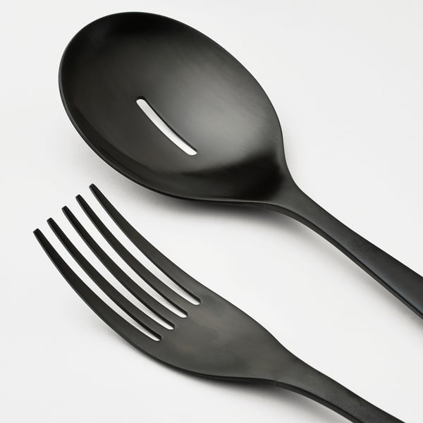 Black stainless steel serving spoon with holes and fork, placed together on a white surface. Sleek and modern design.