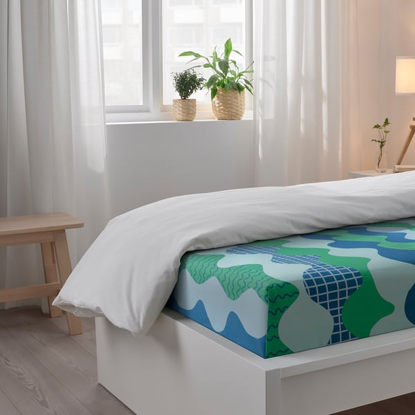 Bright bedroom with white bed, colourful bedding, and plants by window.