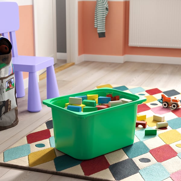 Green storage bin with colourful blocks on chequered mat.